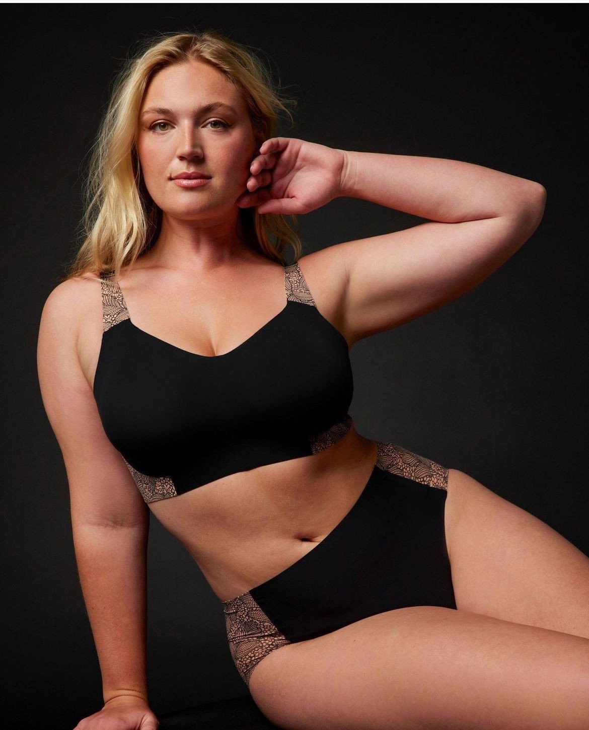 Woman wearing black lingerie with lace accents, posing against a dark background.